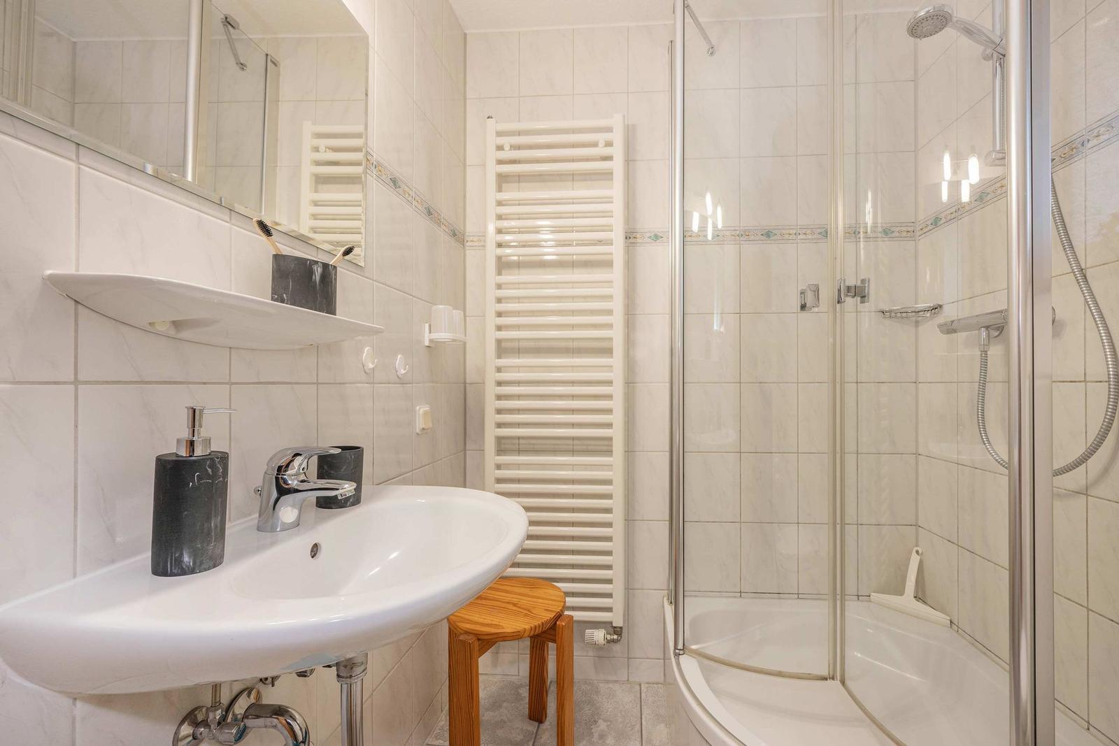 Badezimmer mit Dusche, Waschbecken und Heizkörper