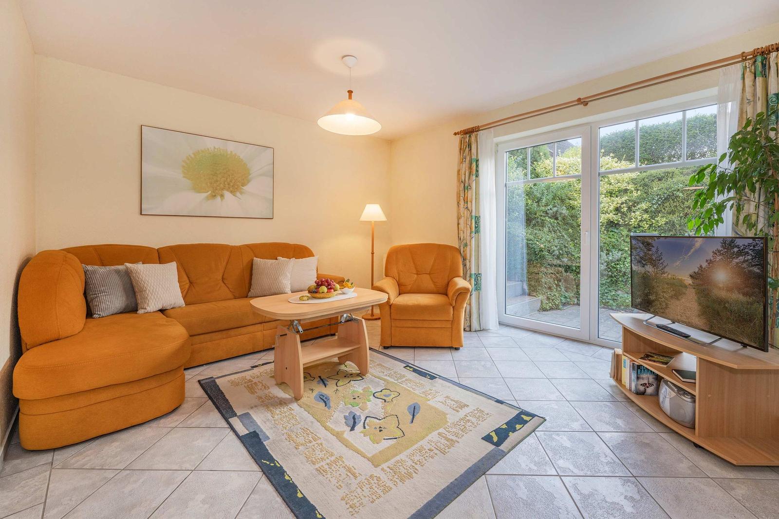 Wohnzimmer mit orangefarbenem Sofa, Sessel, TV und Glastür zur Terrasse.