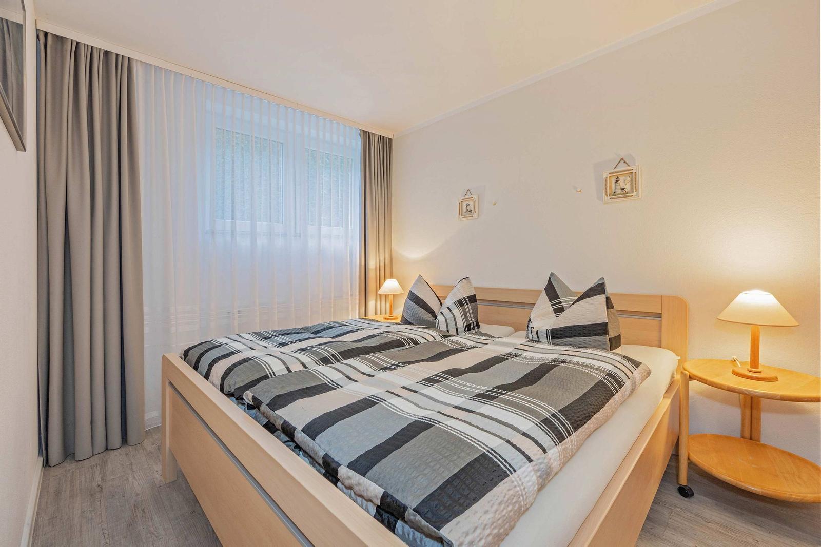 Schlafzimmer mit Doppelbett, Holzgestell, Vorhang und Nachttisch mit Lampe.