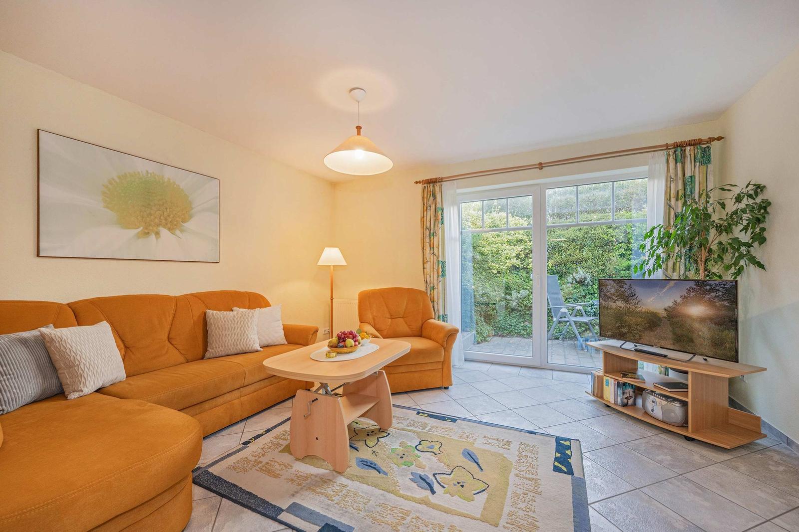 Wohnzimmer mit orange Sofa, Fernseher und Glastür zum Garten.