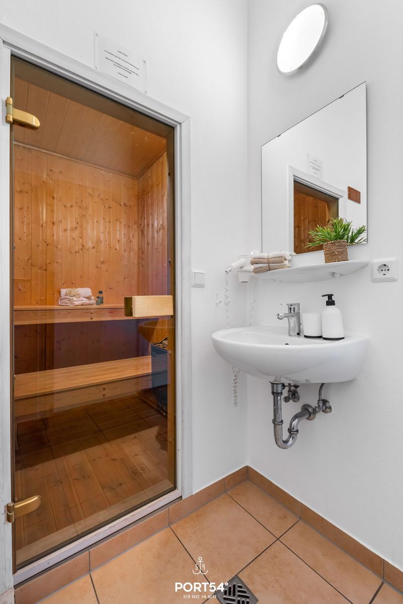 Shower with sauna, sink and mirror. Wooden paneling and floor tiles.