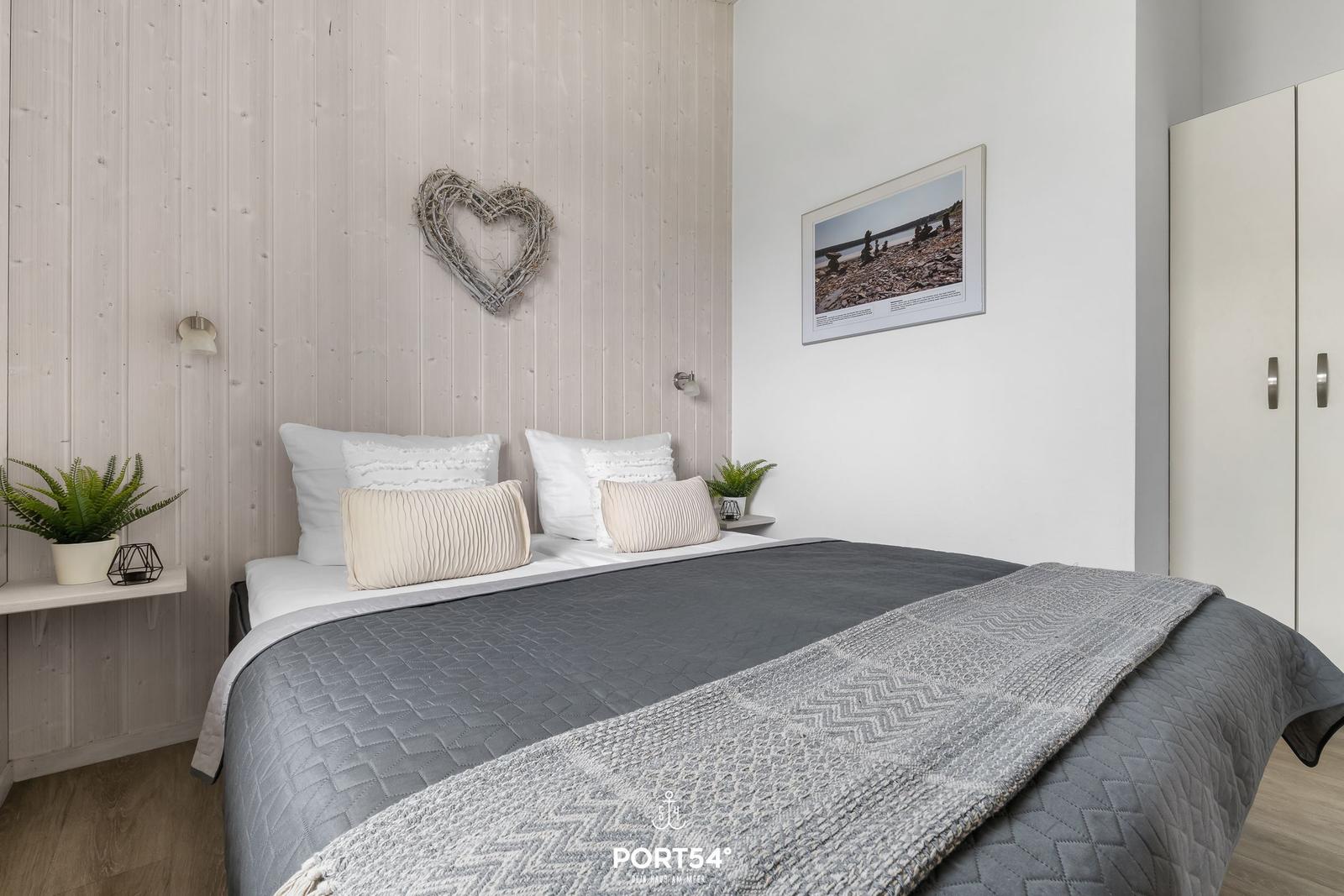 Bedroom with bed, wall art, and wardrobe. Wooden wall and plants provide comfort.