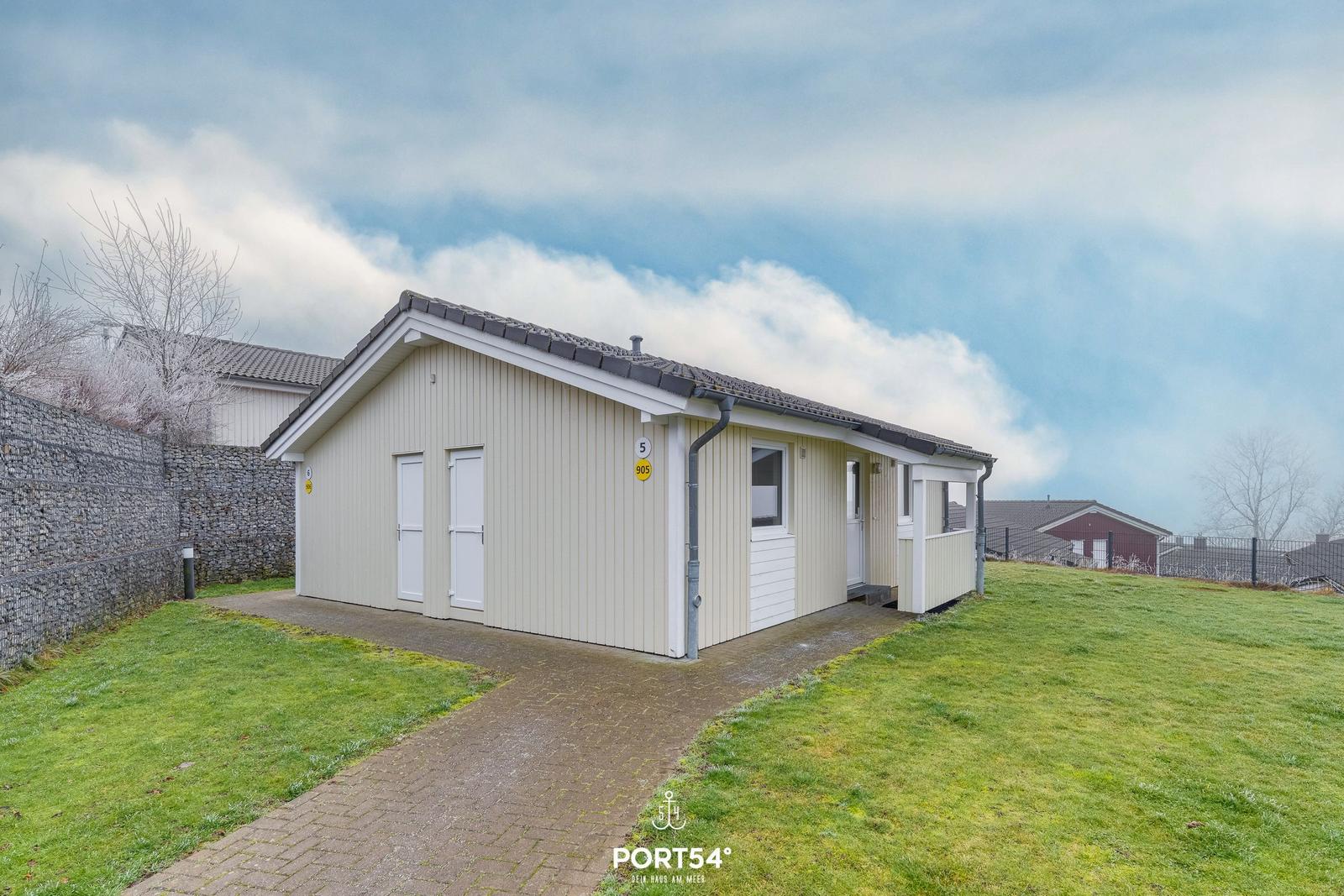A light-colored holiday home with roof, door, and window. Lawn and paved path.
