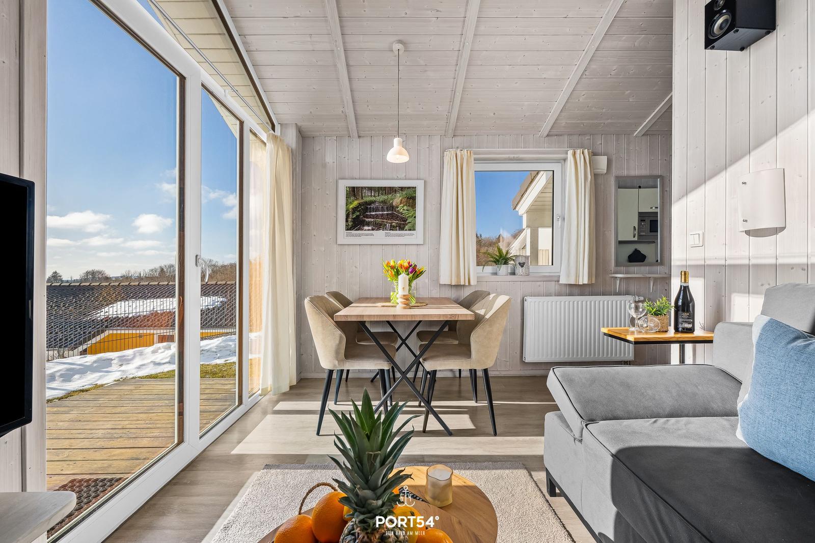 Living and dining area with table, chairs, and sofa. Large windows overlooking the terrace.