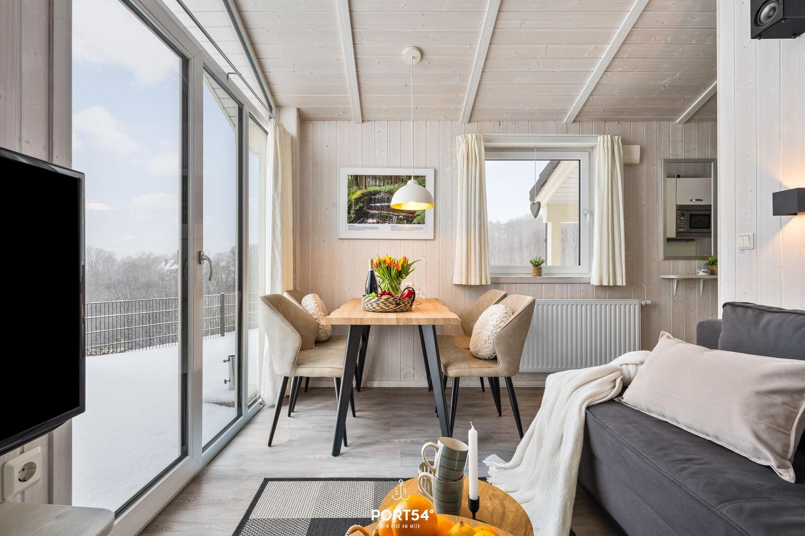 Wohn- und Essbereich mit Tisch, Stühlen und Sofa. Große Glasfront mit Blick auf Schnee.