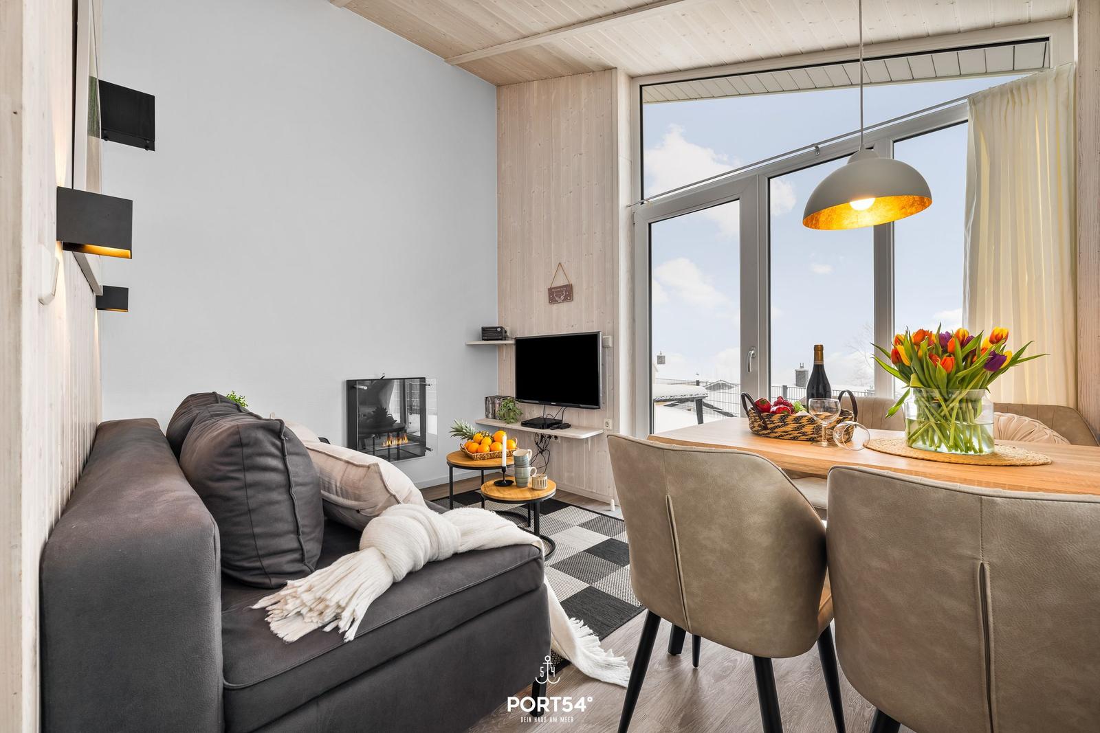 Wohn- und Essbereich mit Sofa, Esstisch und großem Fenster. Holzdecke und Wandverkleidung.