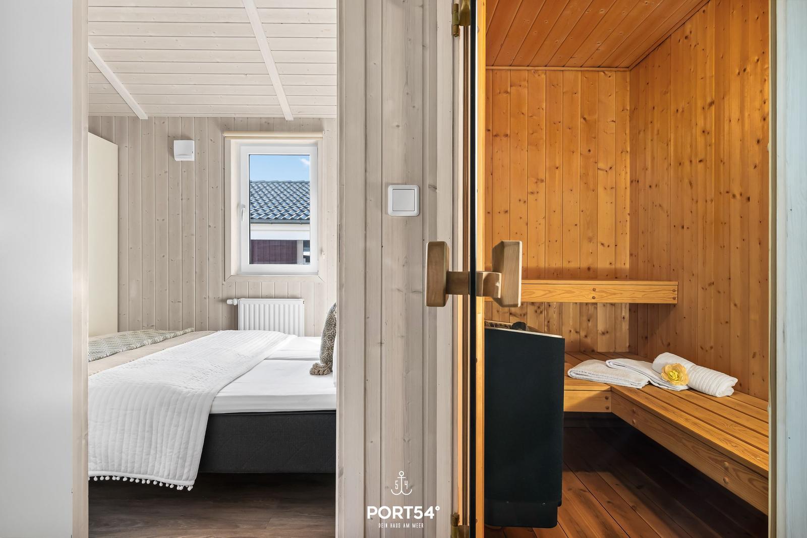 Schlafzimmer mit Bett und Fenster. Sauna mit Holzbank und Handtuch.