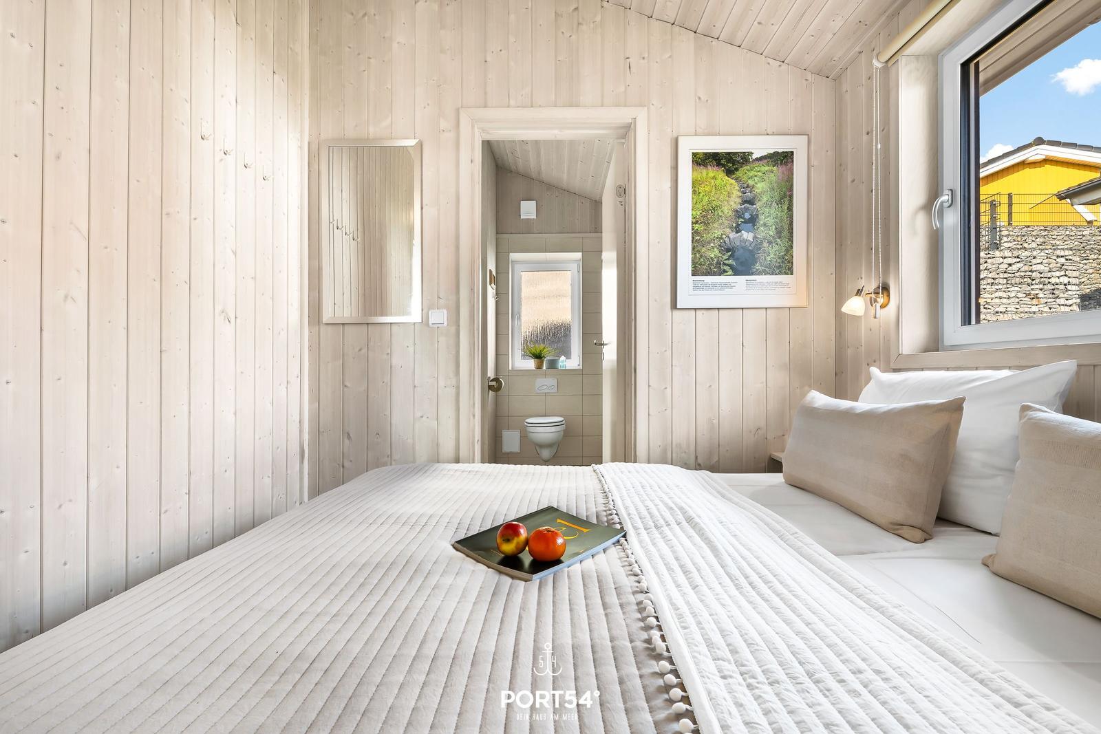 Schlafzimmer mit Holzwand, Bett und Blick auf Außenbereich.