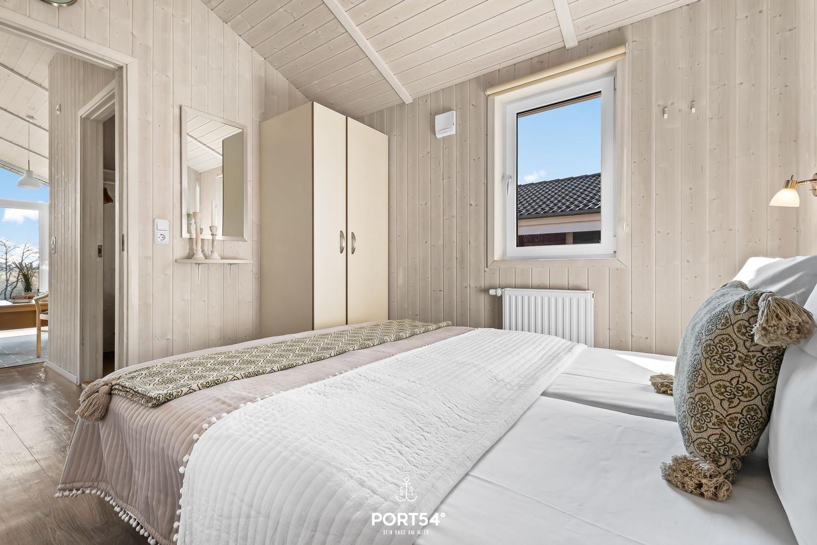Schlafzimmer mit Bett, Kleiderschrank und Fenster. Holzwände und Dachschrägen.