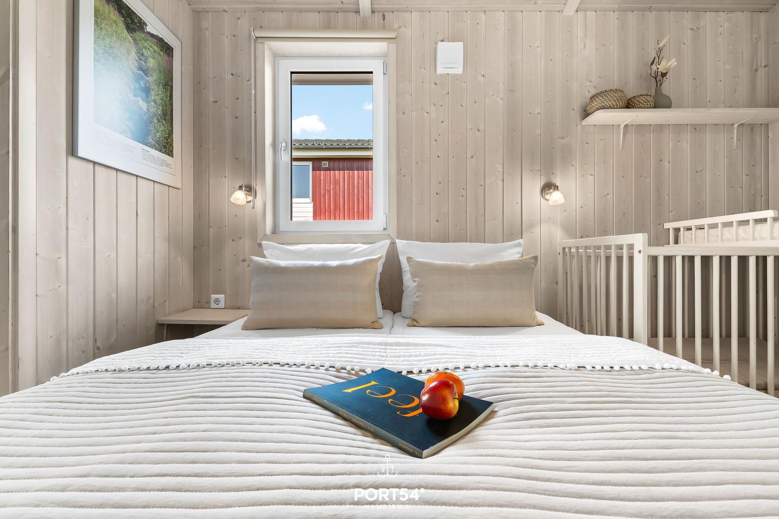Schlafzimmer mit Bett, Kinderbett und Fensterblick auf roten Schuppen.