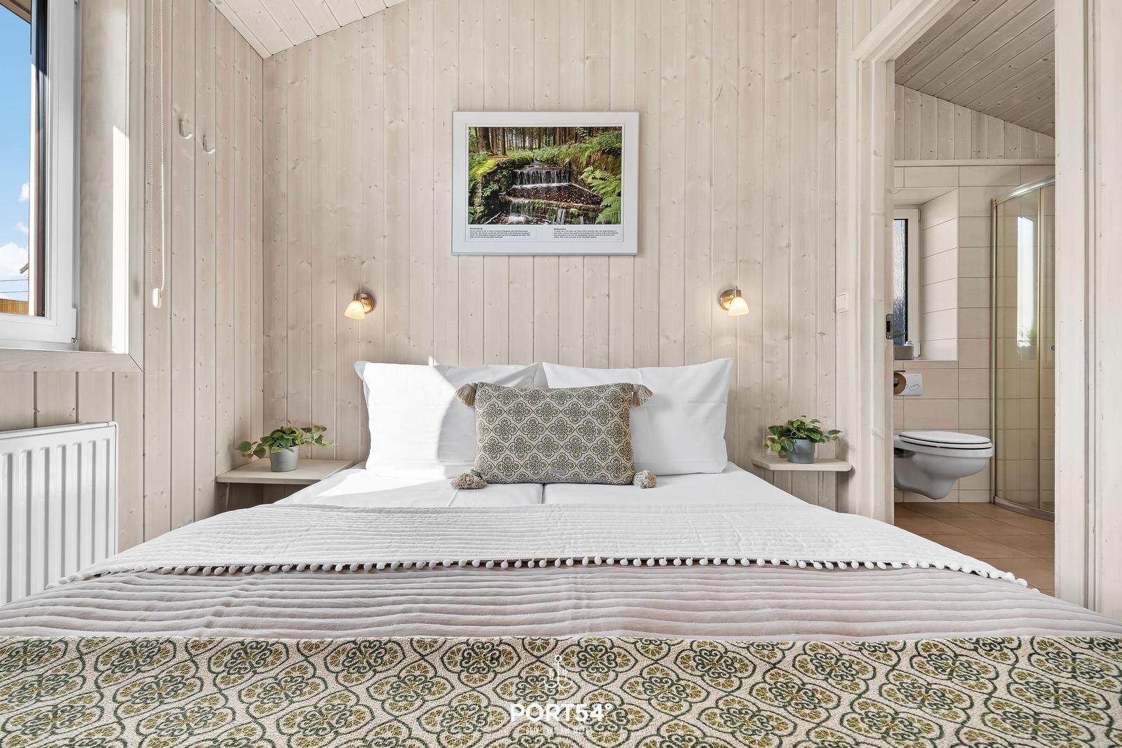 Schlafzimmer mit Holzwand, Bett und Blick in die Badewanne.
