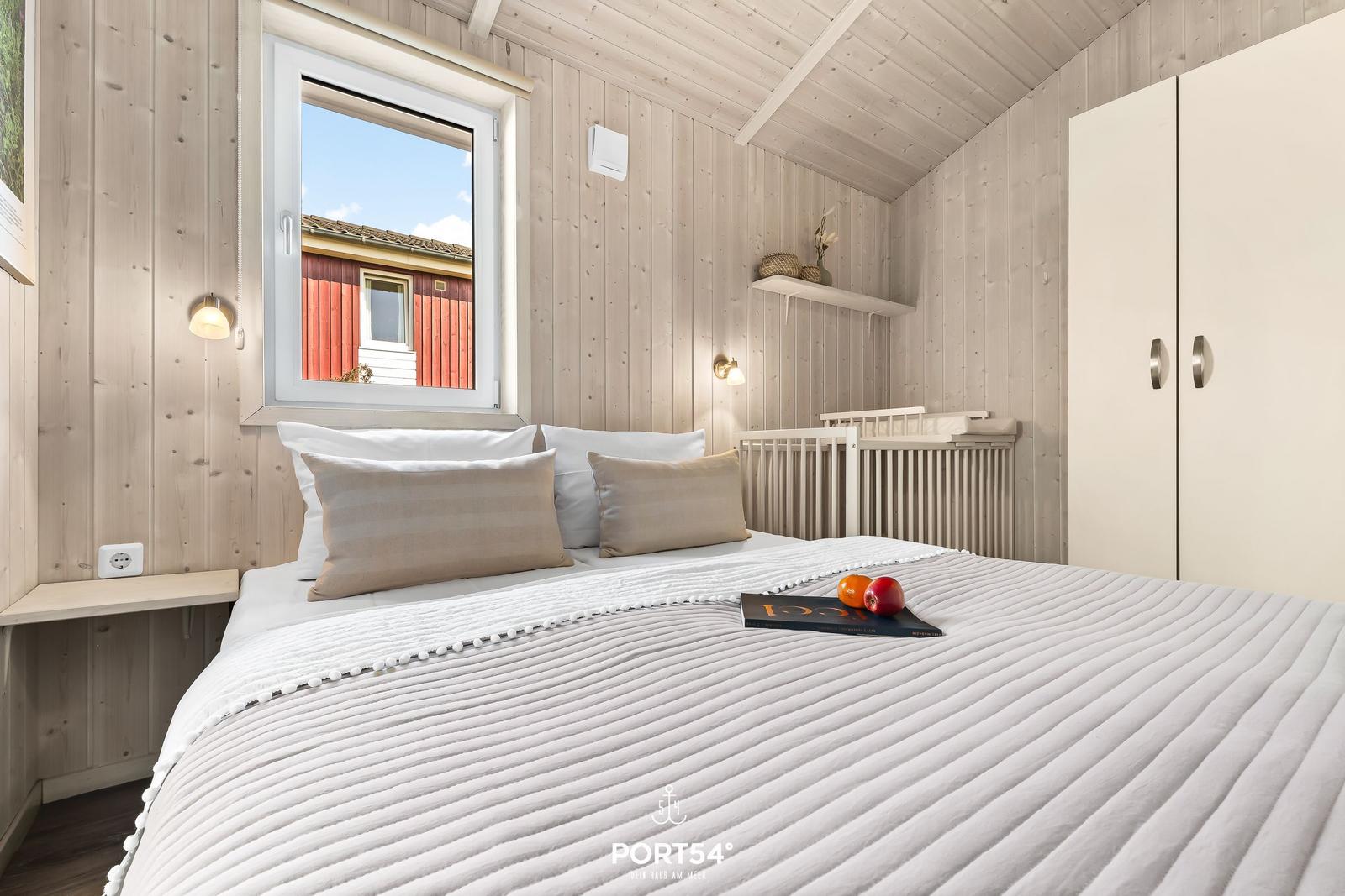 Schlafzimmer mit Bett, Kleiderschrank und Fensterblick auf rotes Haus.