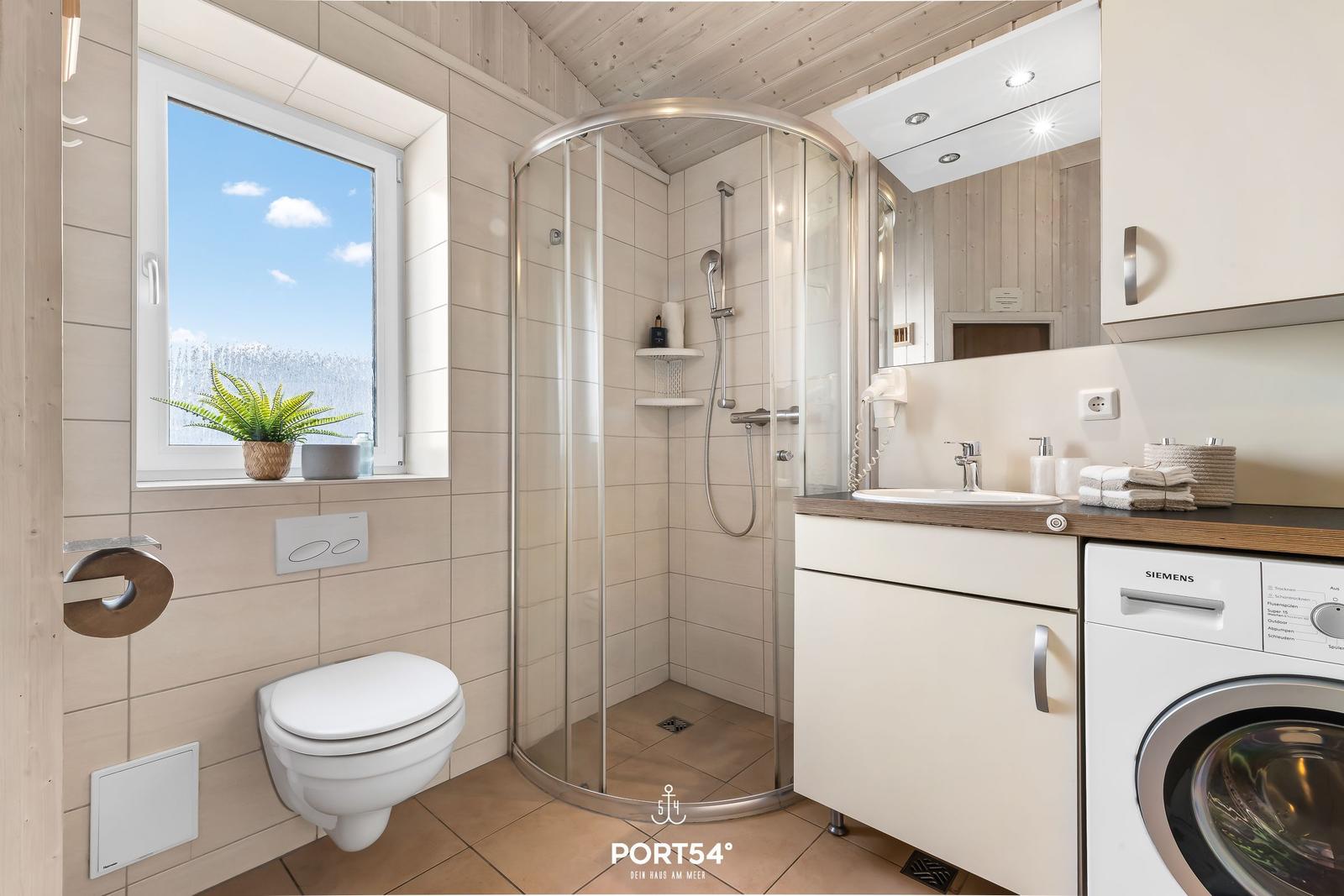 Badezimmer mit Dusche, Waschbecken und Waschmaschine. Fenster mit Blick auf Schnee.