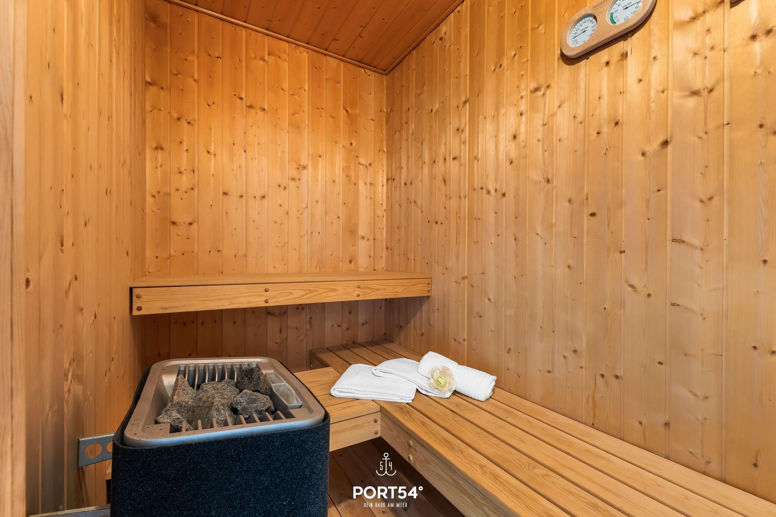 Sauna mit Holzwand, Sitzbank und Steinkessel mit Handtuch.