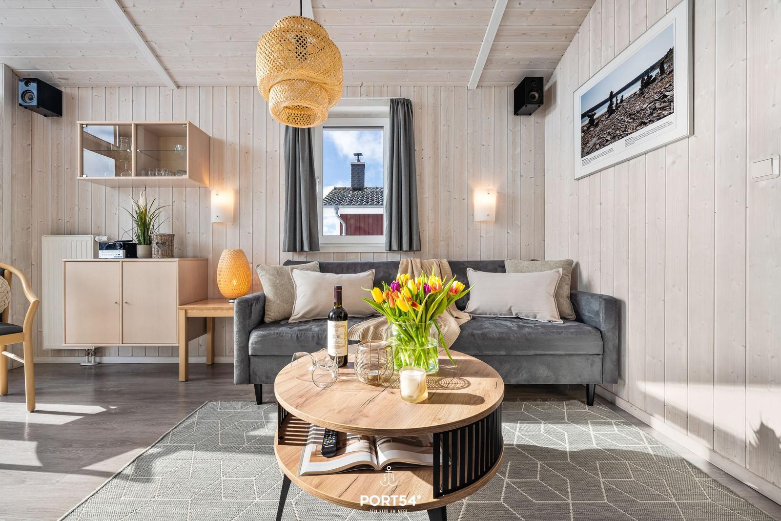 Wohnzimmer mit grauem Sofa, Holztisch und Fensterblick auf Haus.