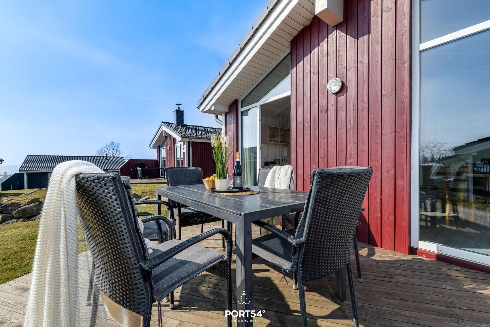 Terrasse mit Tisch und Stühlen vor rotem Holzhaus. Blick auf Garten und Nachbarhaus.