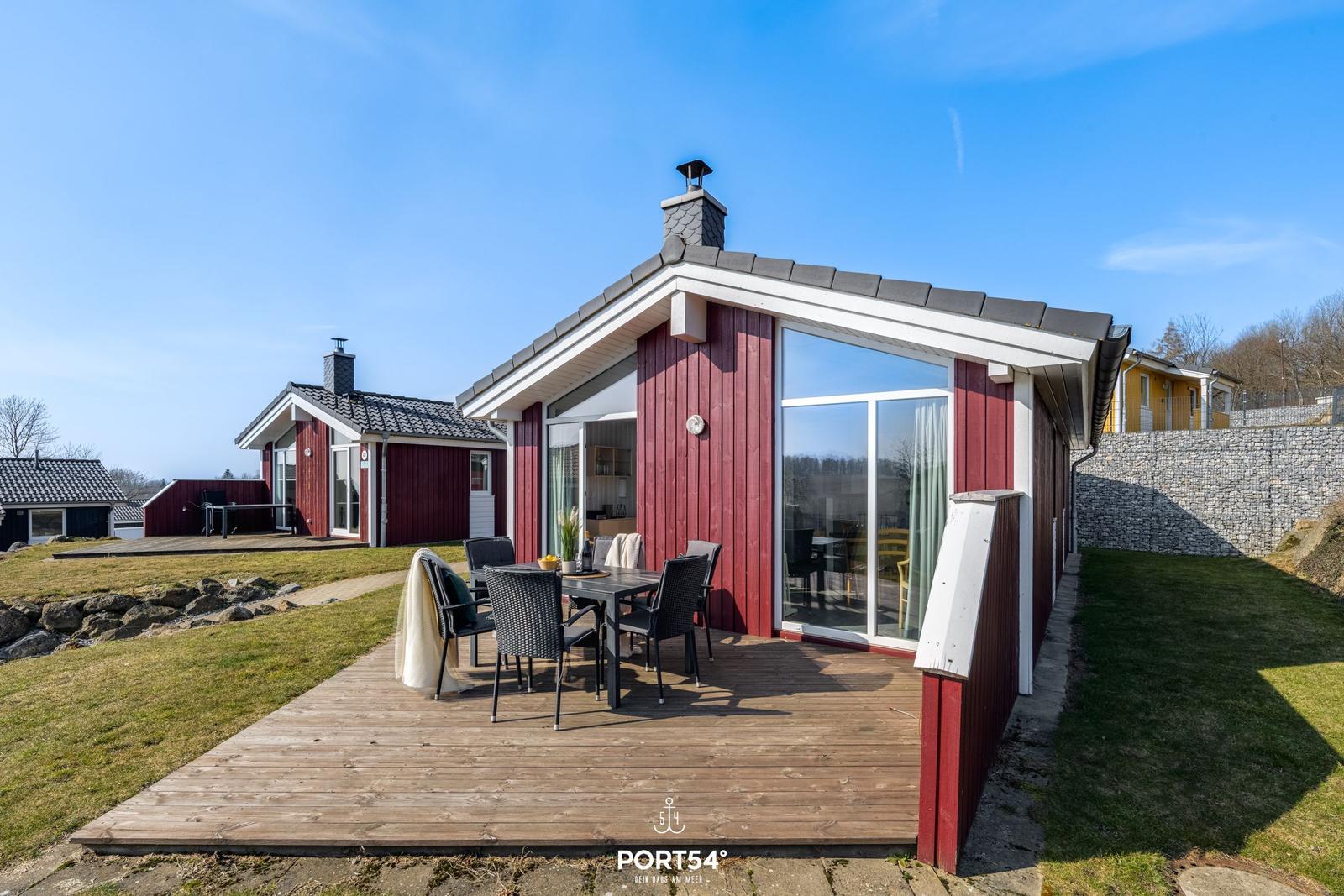 Rotes Ferienhaus mit Terrasse und Garten. Glastüren führen ins Innere.