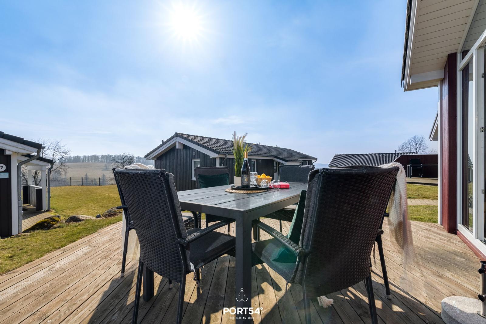 Terrasse mit Tisch und Stühlen, Blick auf Wohnhaus und Grünland.