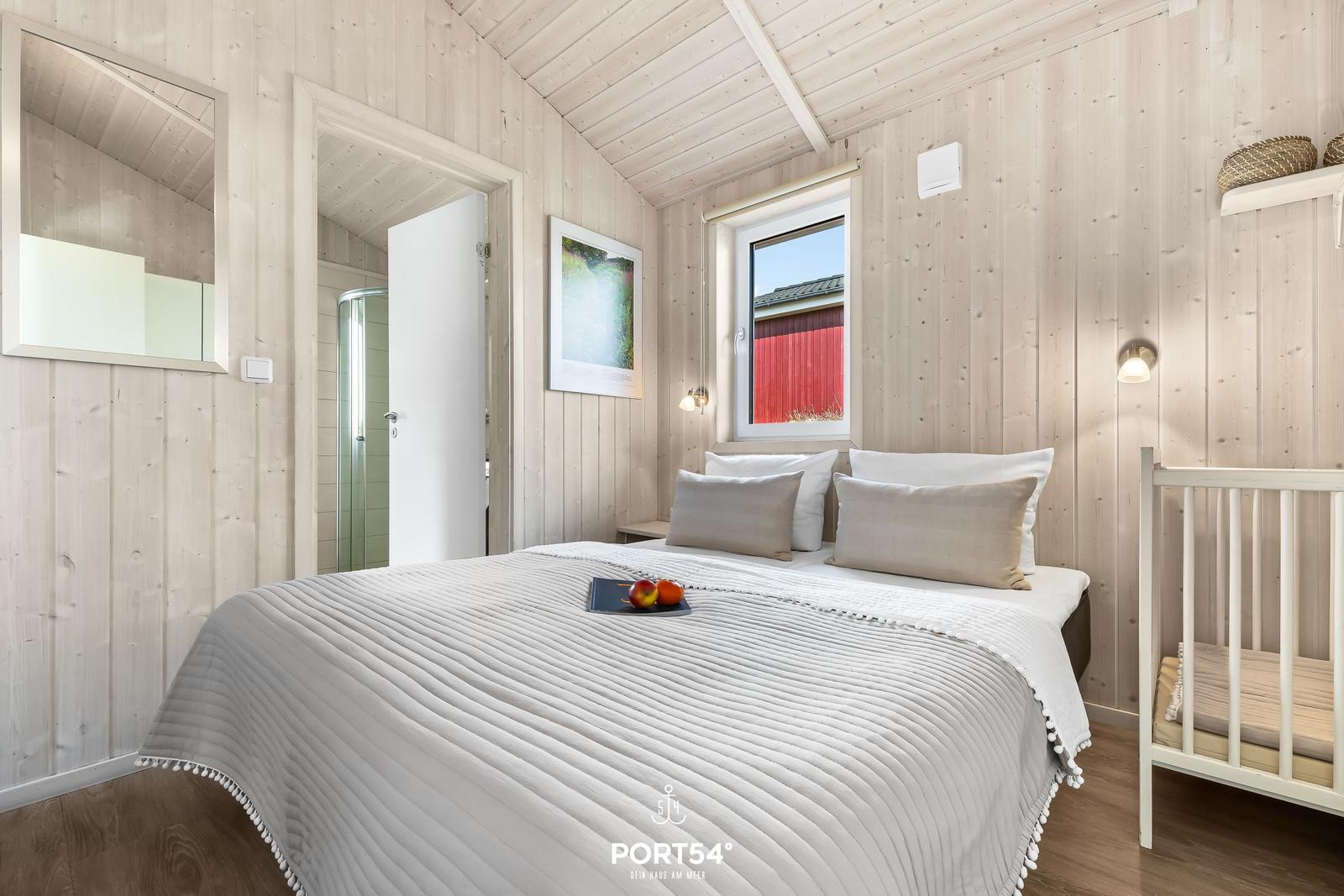 Schlafzimmer mit Bett, Kinderbett und Dusche im Hintergrund.