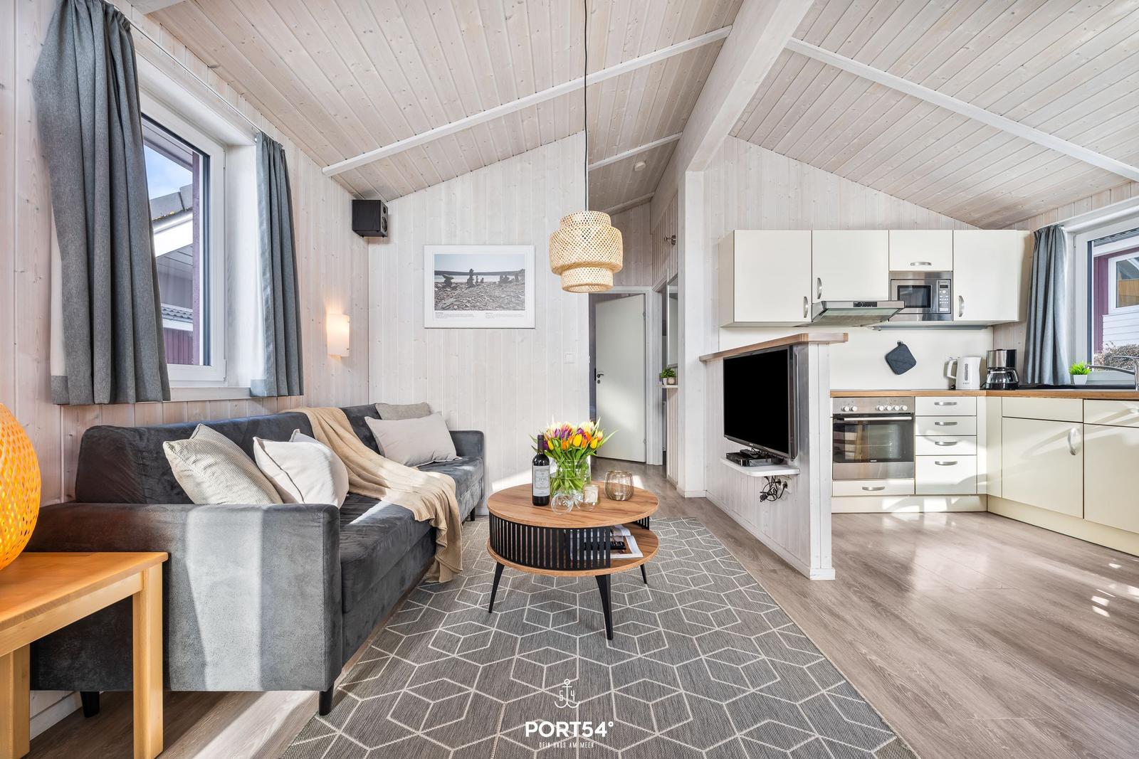 Wohnzimmer mit Sofa, Couchtisch und Küchenbereich unter Holzdecke.