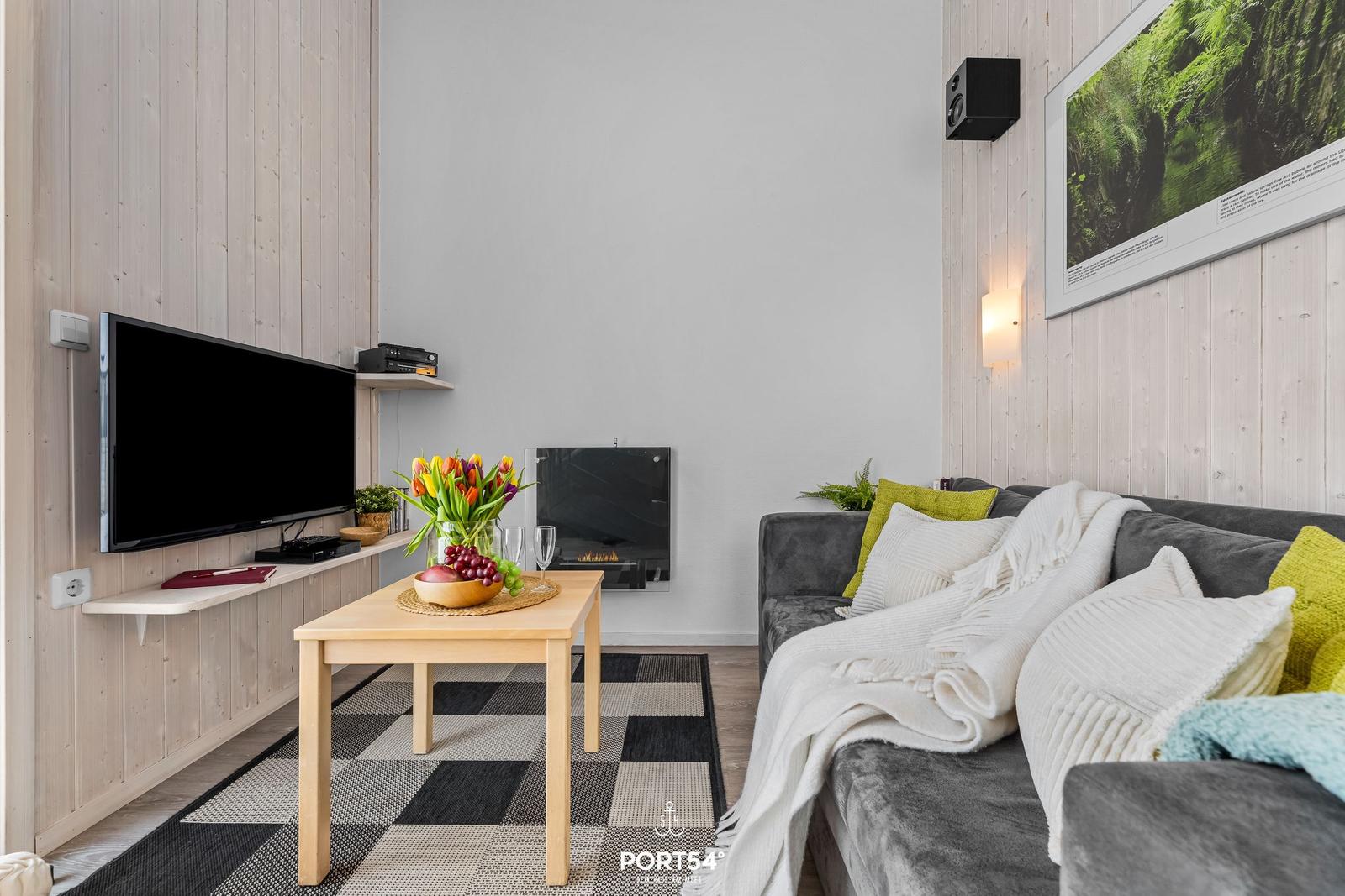 Wohnzimmer mit Sofa, Fernseher, Kamin und Tisch mit Blumen.