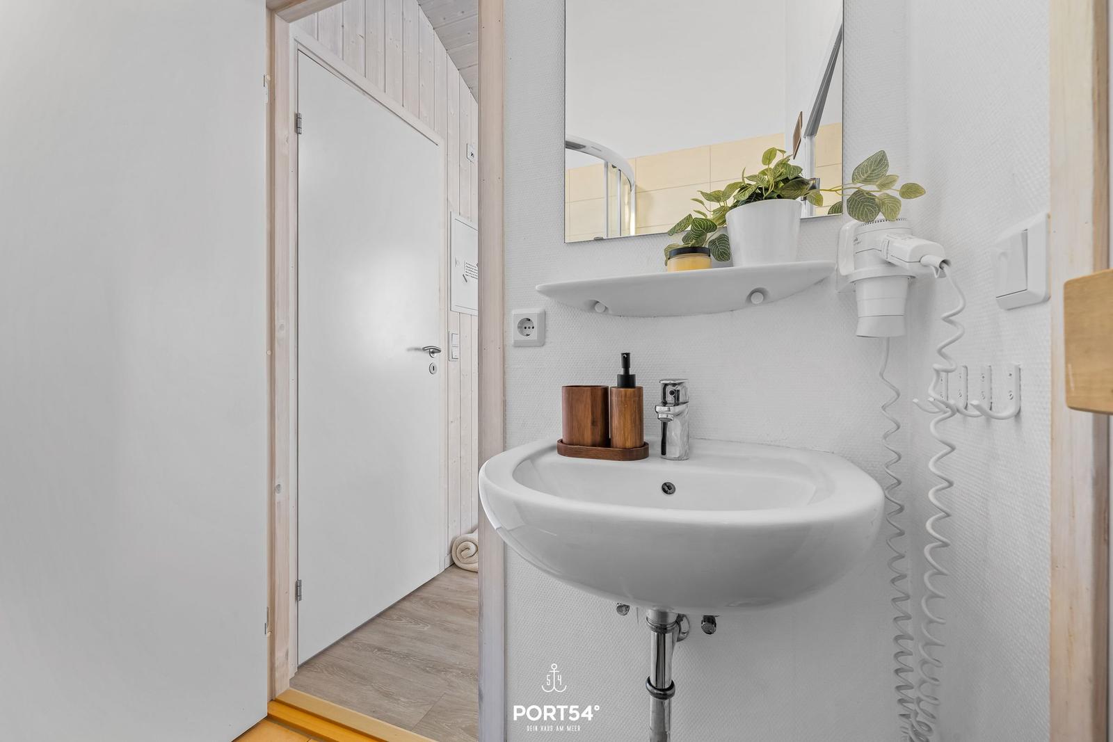 Waschbecken mit Spiegel, Pflanze und Handtuchhalter in einem Badezimmer.