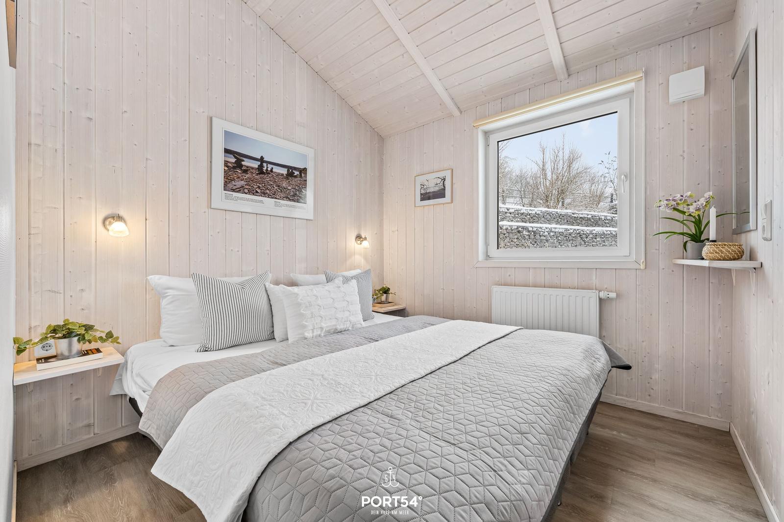 Schlafzimmer mit Bett, Fenster und Holzwandverkleidung.