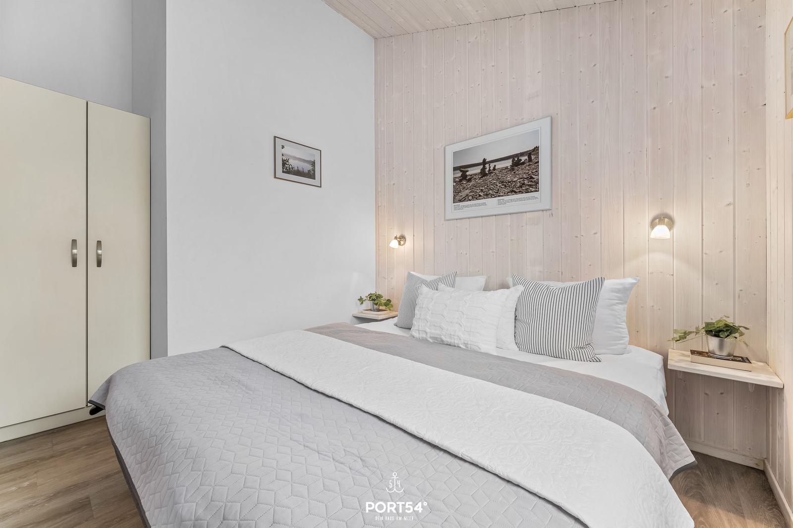 Schlafzimmer mit Bett, Kleiderschrank und Holzwand. Zwei Nachttische mit Pflanzen.