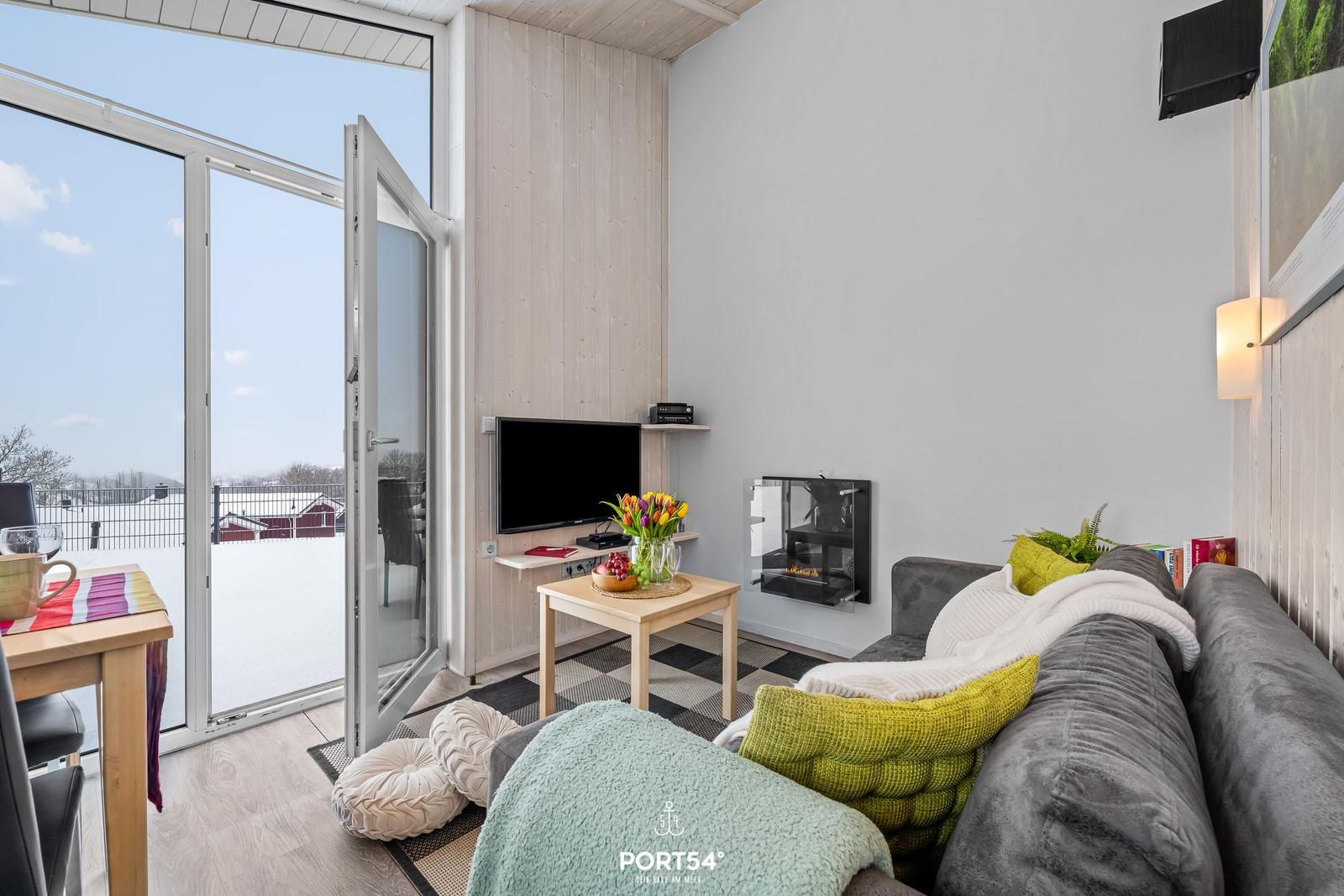 Wohnzimmer mit Sofa, Fernseher und Blick auf verschneiten Balkon.