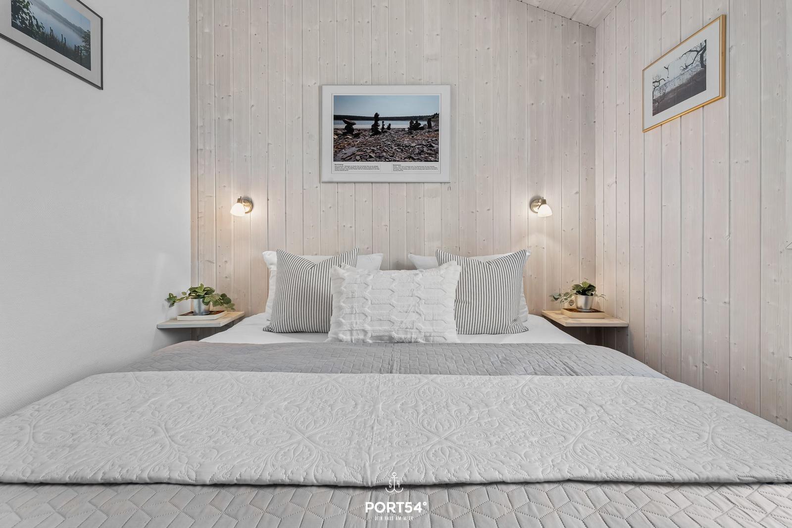 Schlafzimmer mit Bett, Wandbildern und Nachttischen mit Pflanzen.