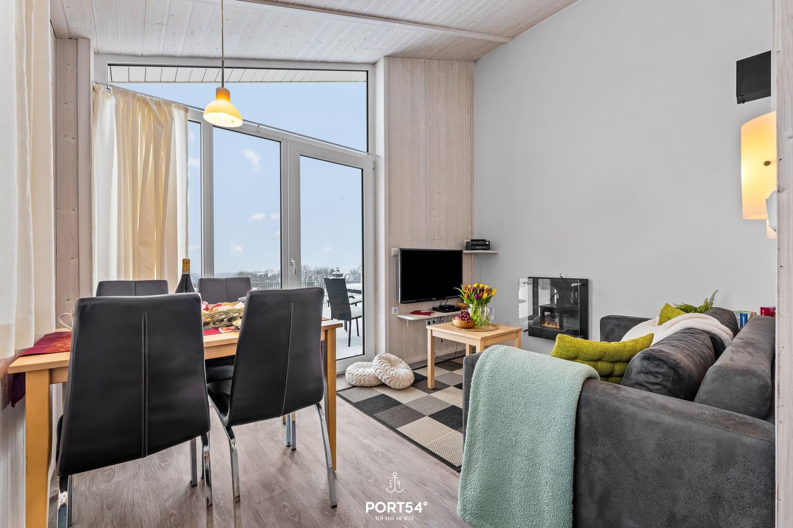 Wohn- und Essbereich mit großem Fenster, Sofa, Fernseher und Kamin.