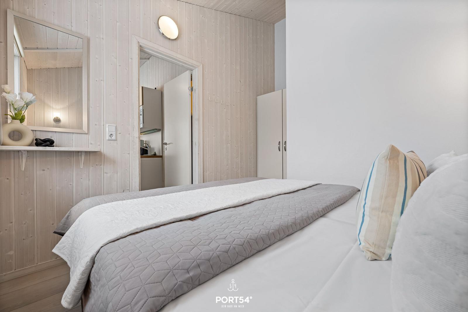 Bedroom with bed, mirror, and wardrobe. Wood wall and door visible.