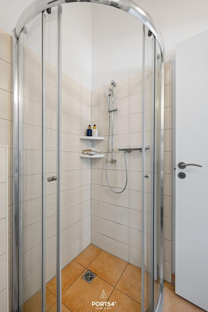 Shower cabin with glass door, shower head, and shelf