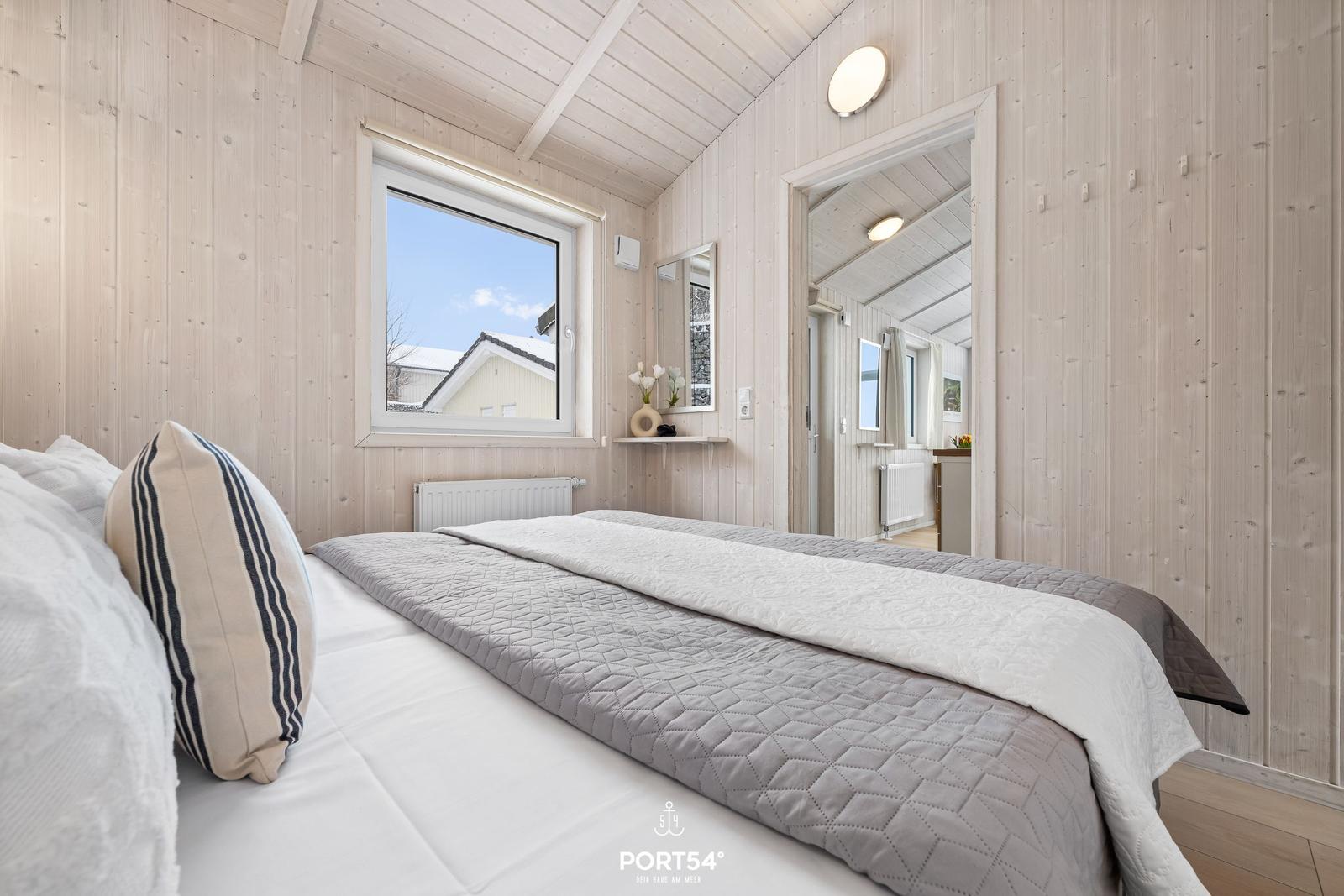 Bedroom with bed, window, and wooden walls. View of roof and sky.