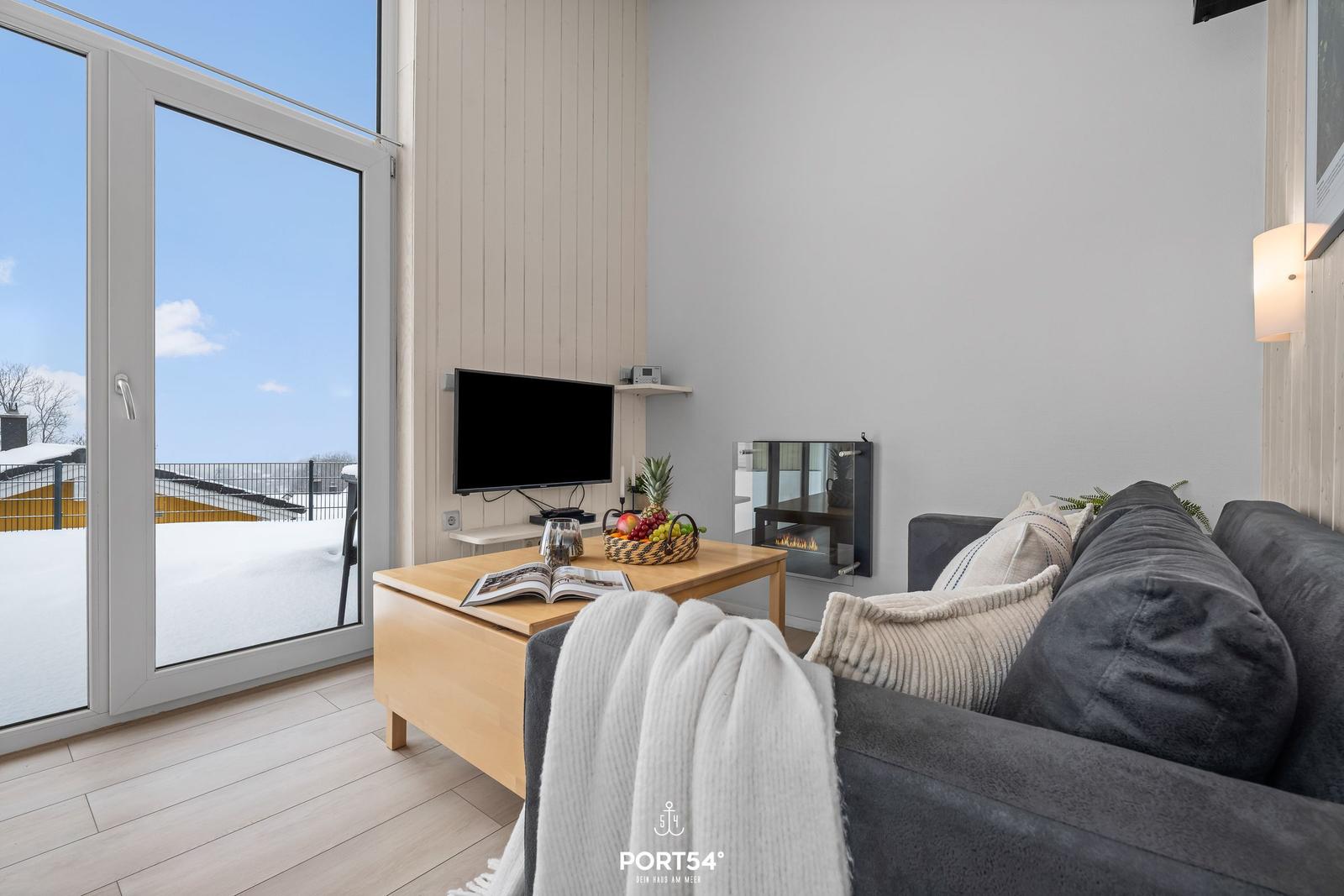 Living room with sofa, TV, and fireplace. Sliding glass door leads to snowy balcony.