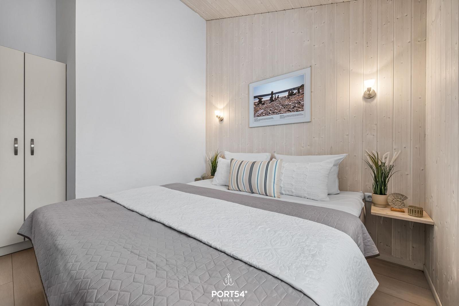 Bedroom with bed, wardrobe, and wooden wall. Picture on wall, lighting, and plants.
