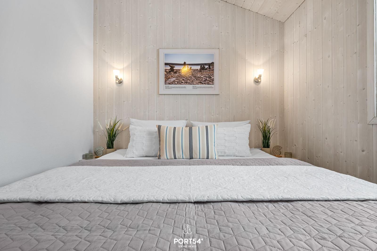 Bedroom with bed, wall art, and wall lamps on wood wall.