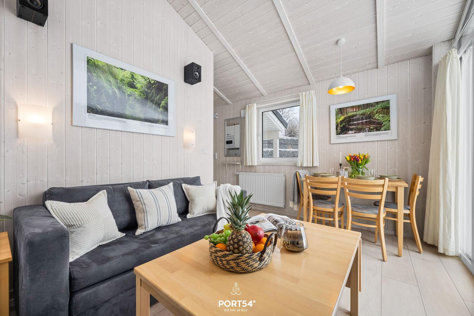 Living and dining area with sofa, table, and chairs. Wooden walls and ceiling. Pictures on the walls.