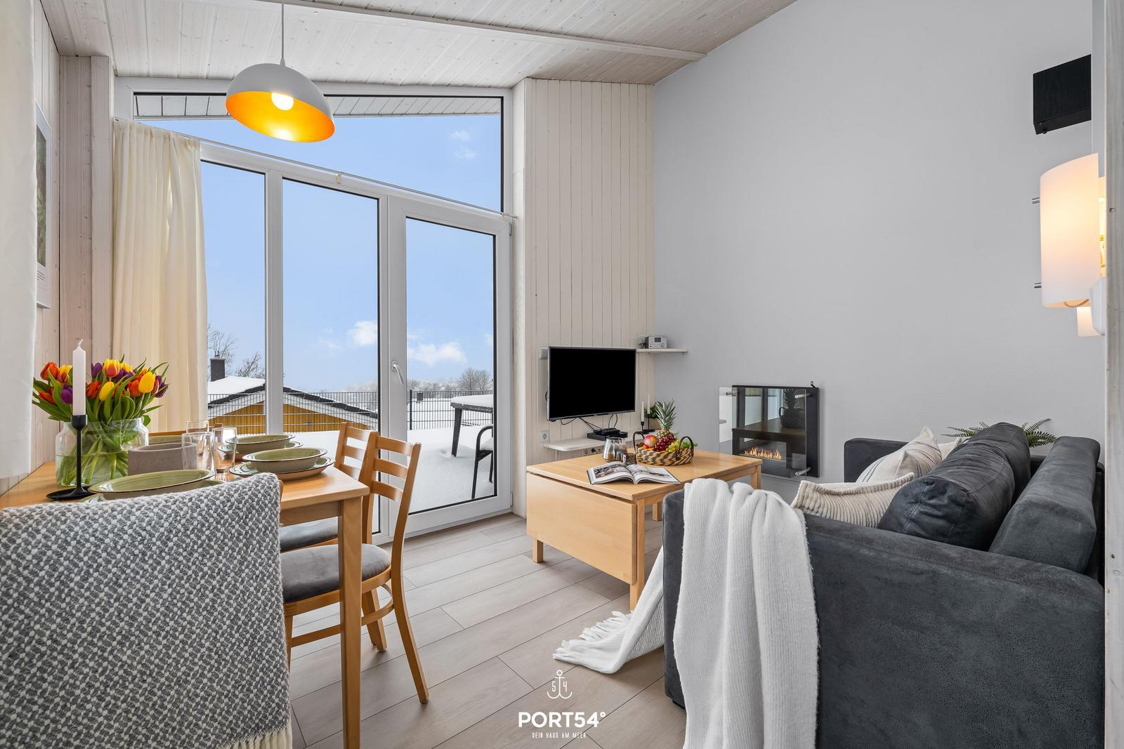 Living and dining area with sofa, dining table, and TV. Large windows with view of the outdoor area.