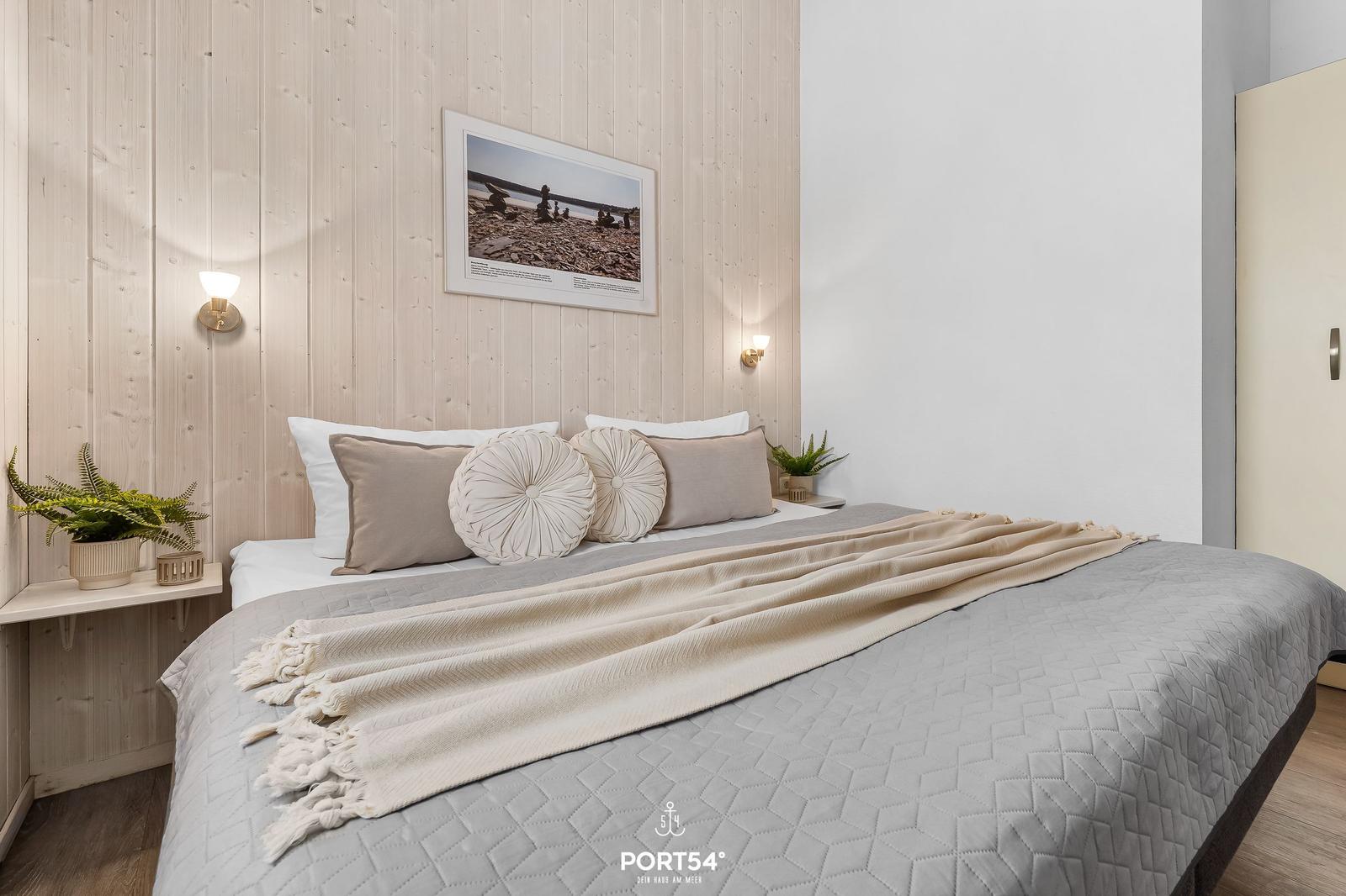 Bedroom with bed, pillows, and blanket. Wooden wall, picture, and plants.