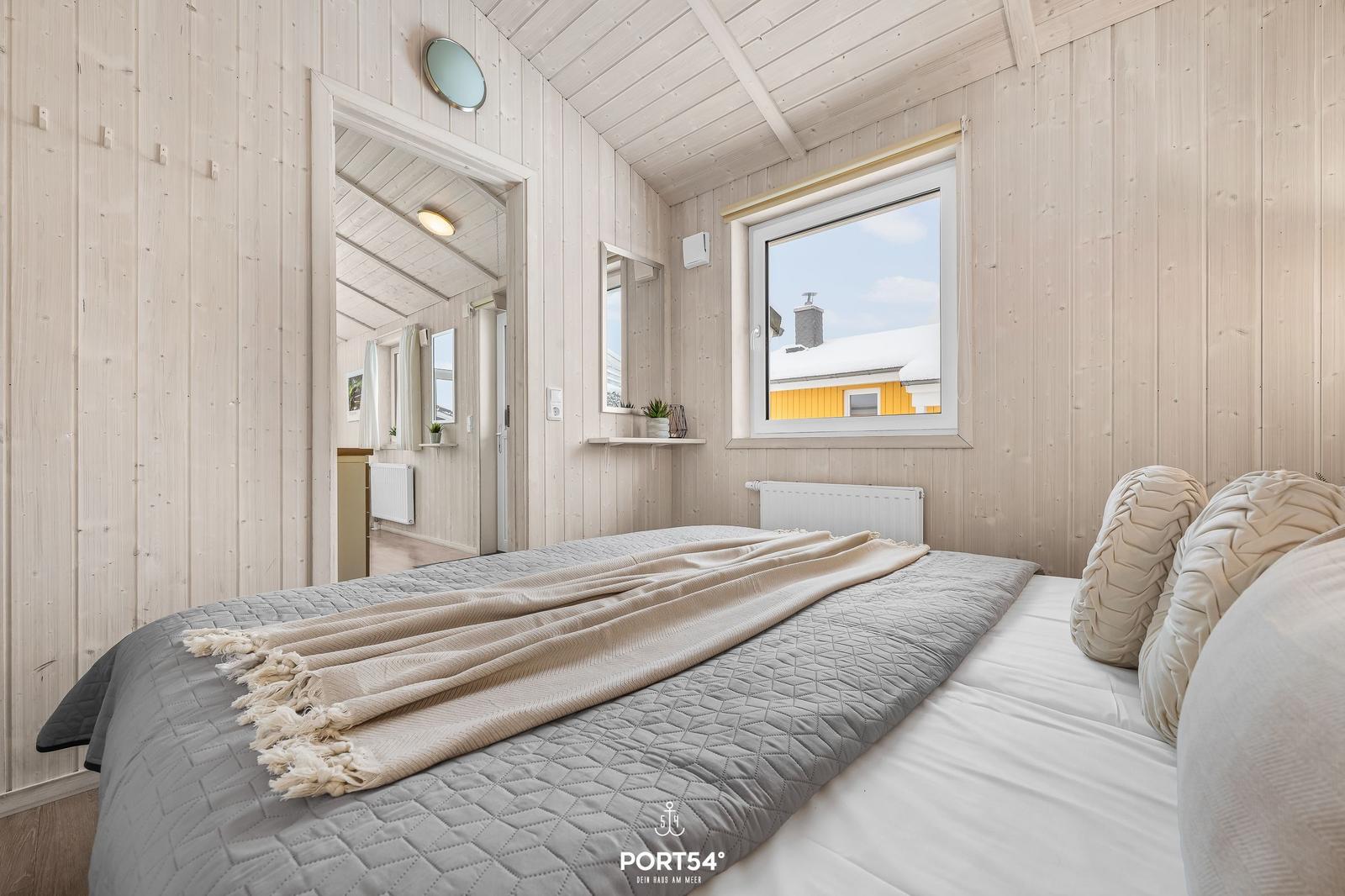Bedroom with wooden walls, bed, and window overlooking house