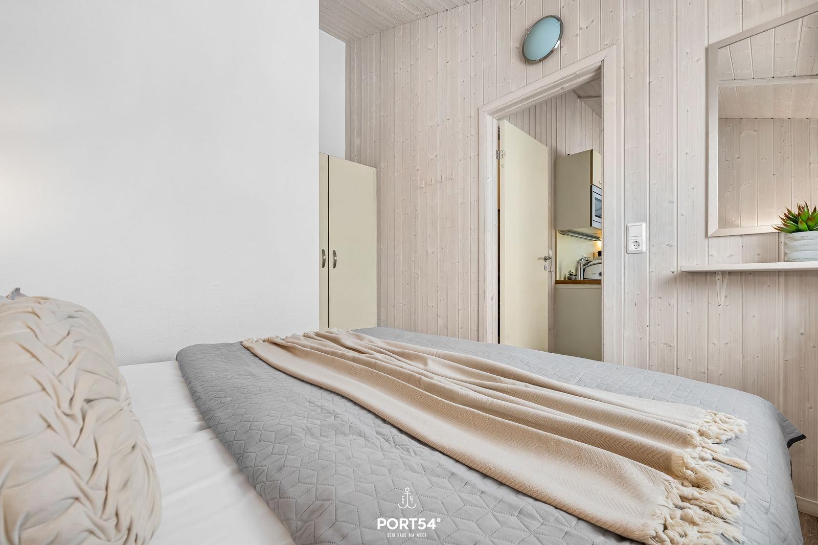 Bedroom with bed, wooden walls, and view into the kitchen.