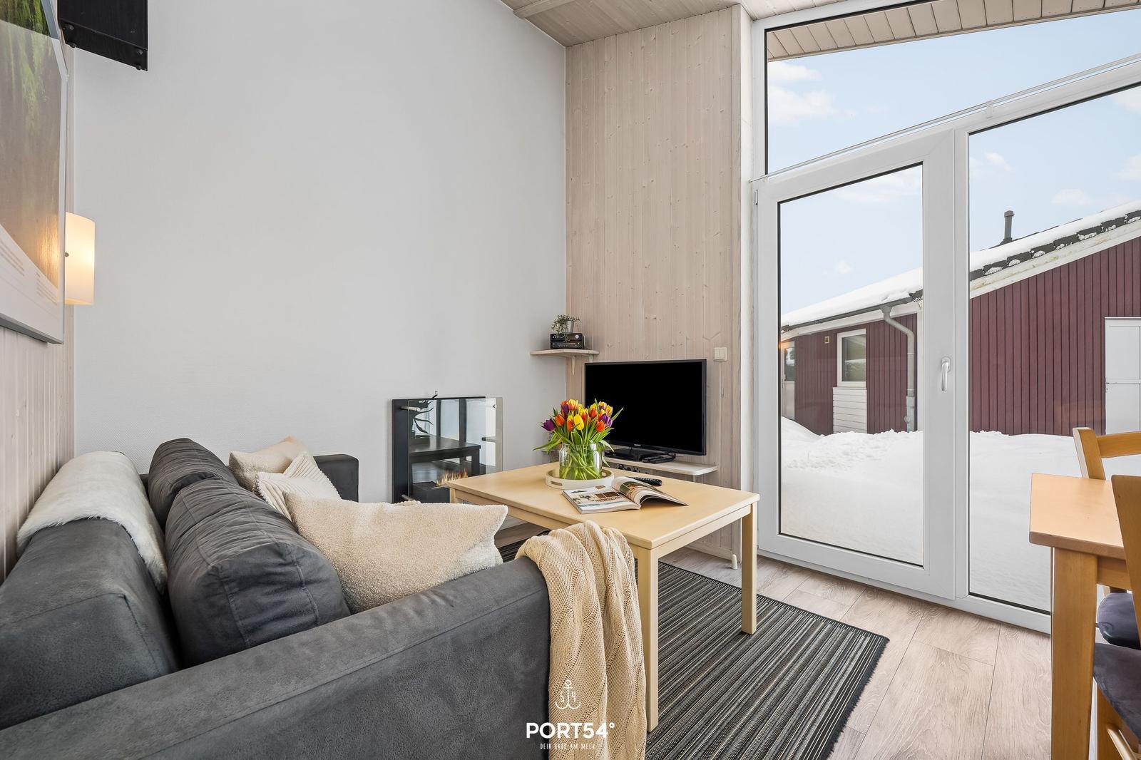 Living room with sofa, coffee table, and TV. Entrance to snowy outdoor terrace.