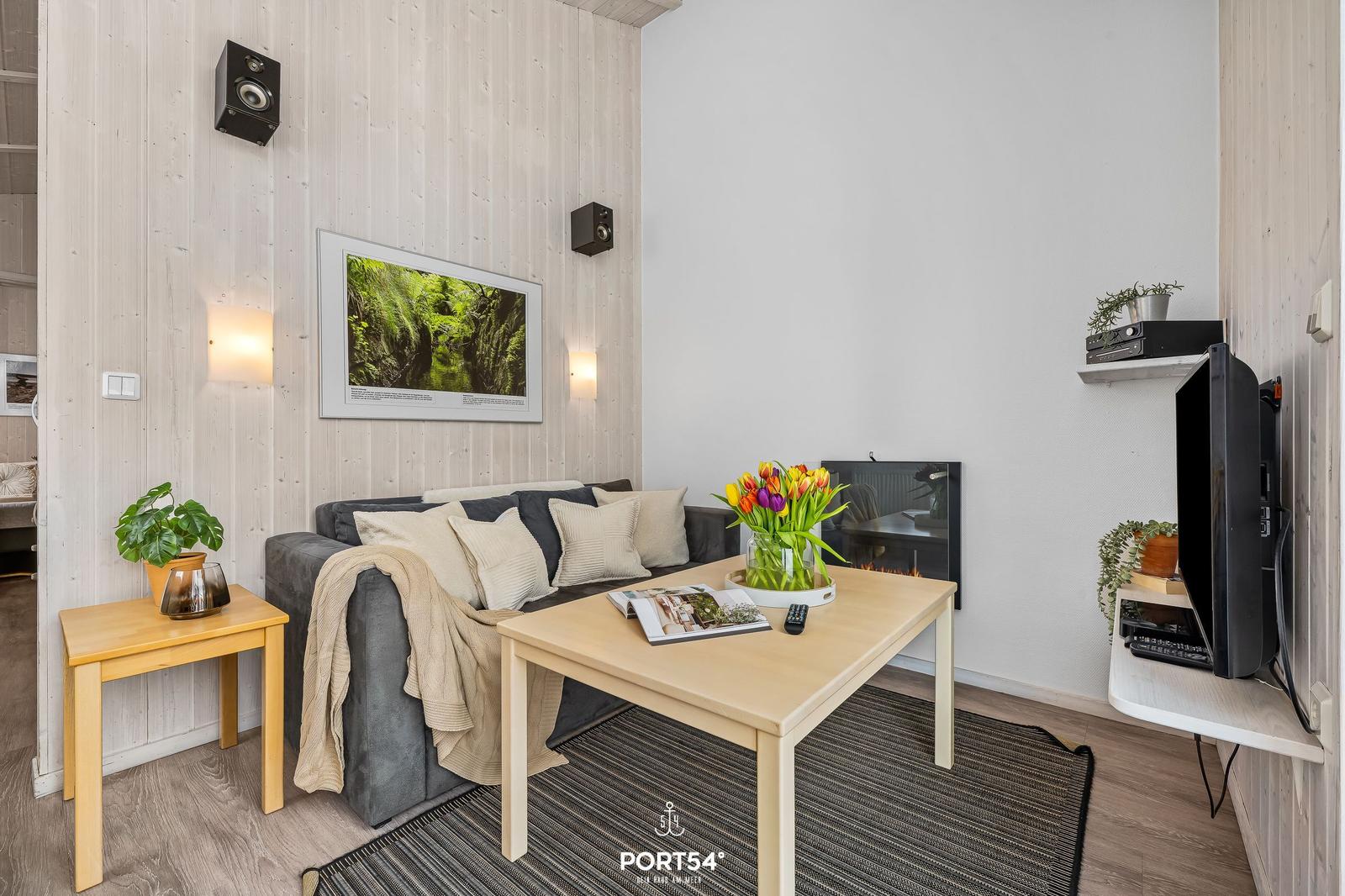 Living room with sofa, table, TV, and fireplace. Wall art and plants create ambiance.