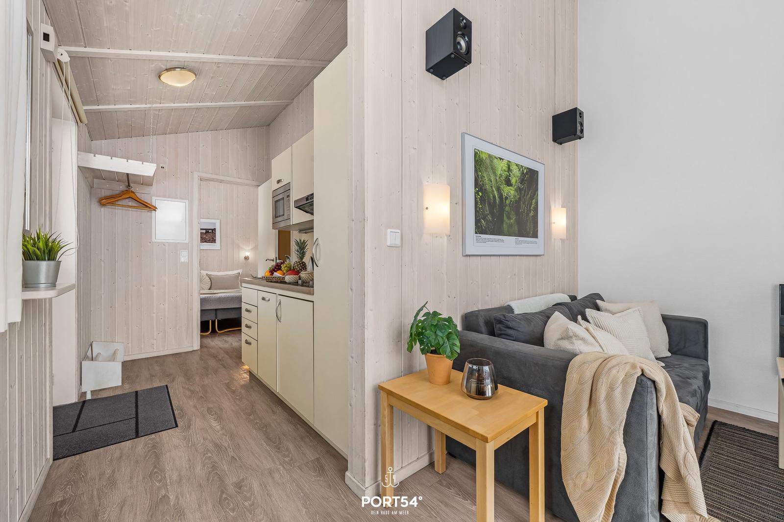 Living area with sofa, kitchenette, and bedroom in the background.