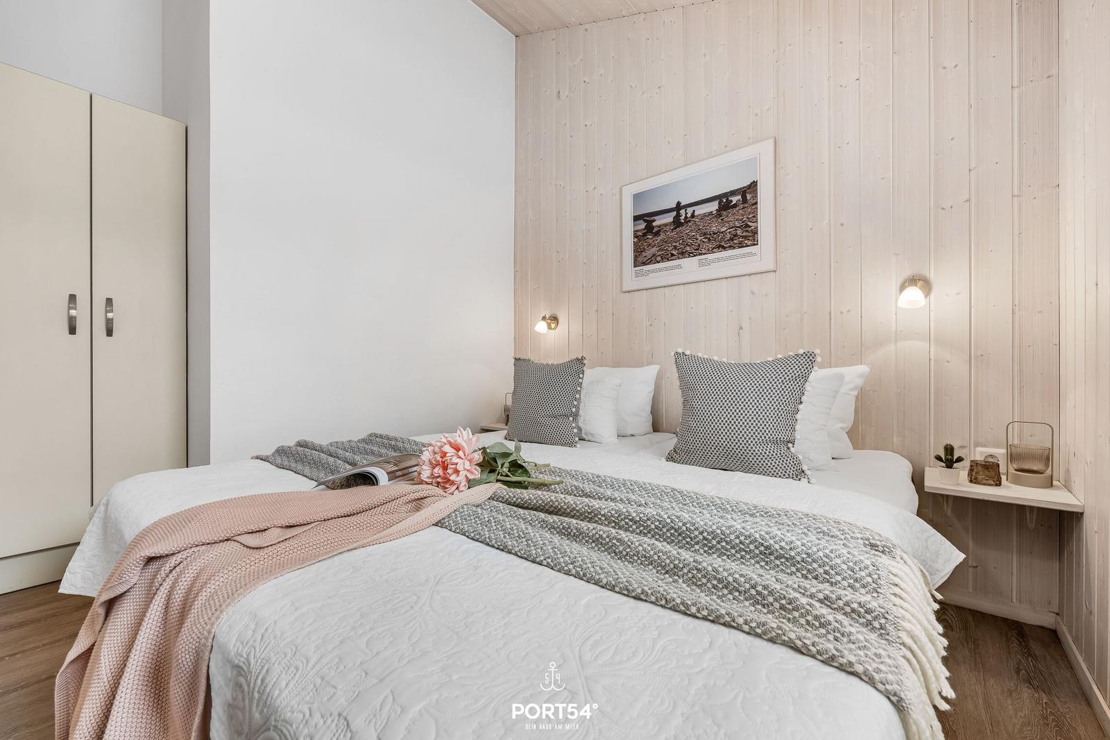 Schlafzimmer mit Bett, Kleiderschrank und Holzwand. Auf dem Bett liegt eine Blume.