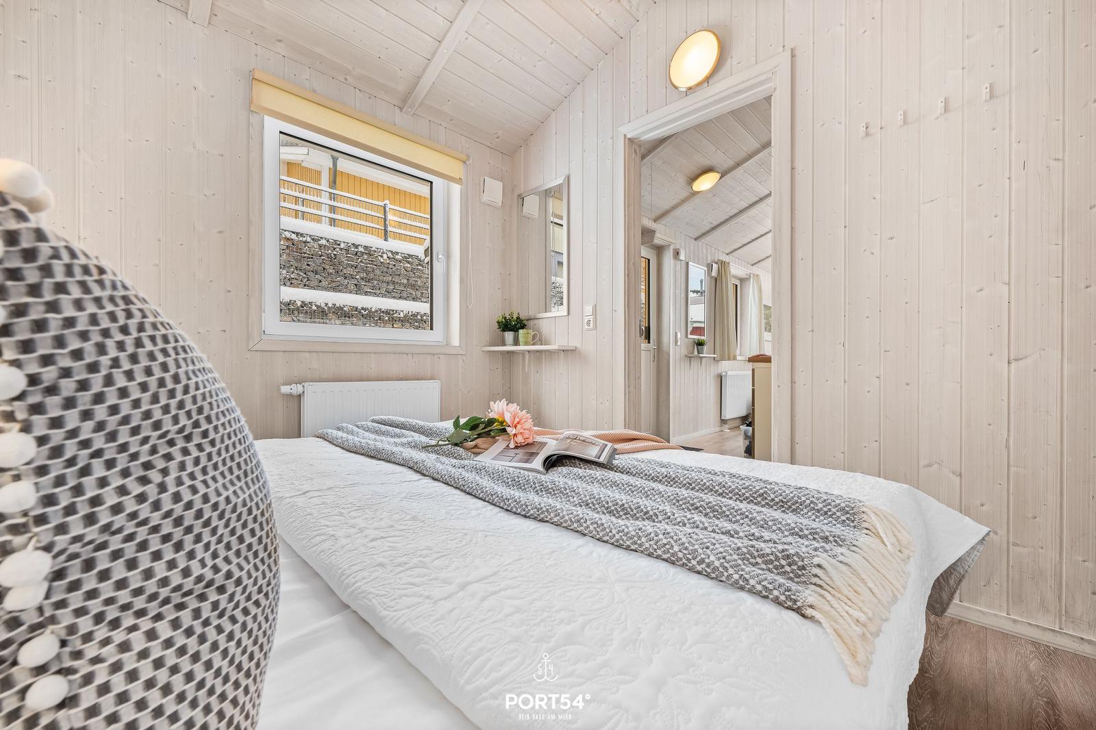 Schlafzimmer mit Bett, Fenster und Blick auf Außenbereich.