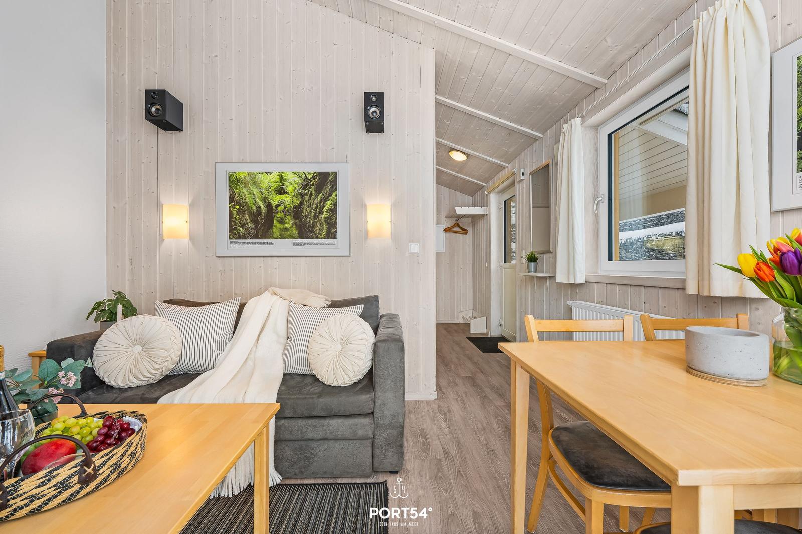 Wohn- und Essbereich mit Sofa, Tisch und Fenster. Holzwände und -boden.