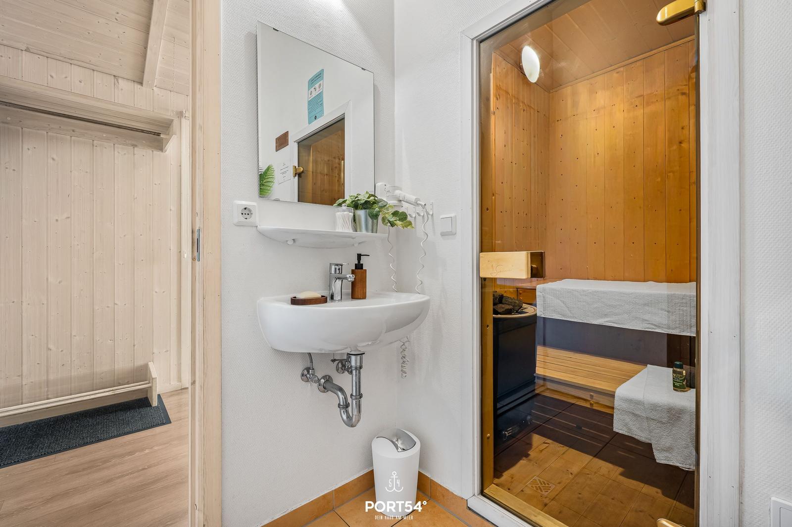 Waschbecken mit Spiegel und Sauna im Hintergrund