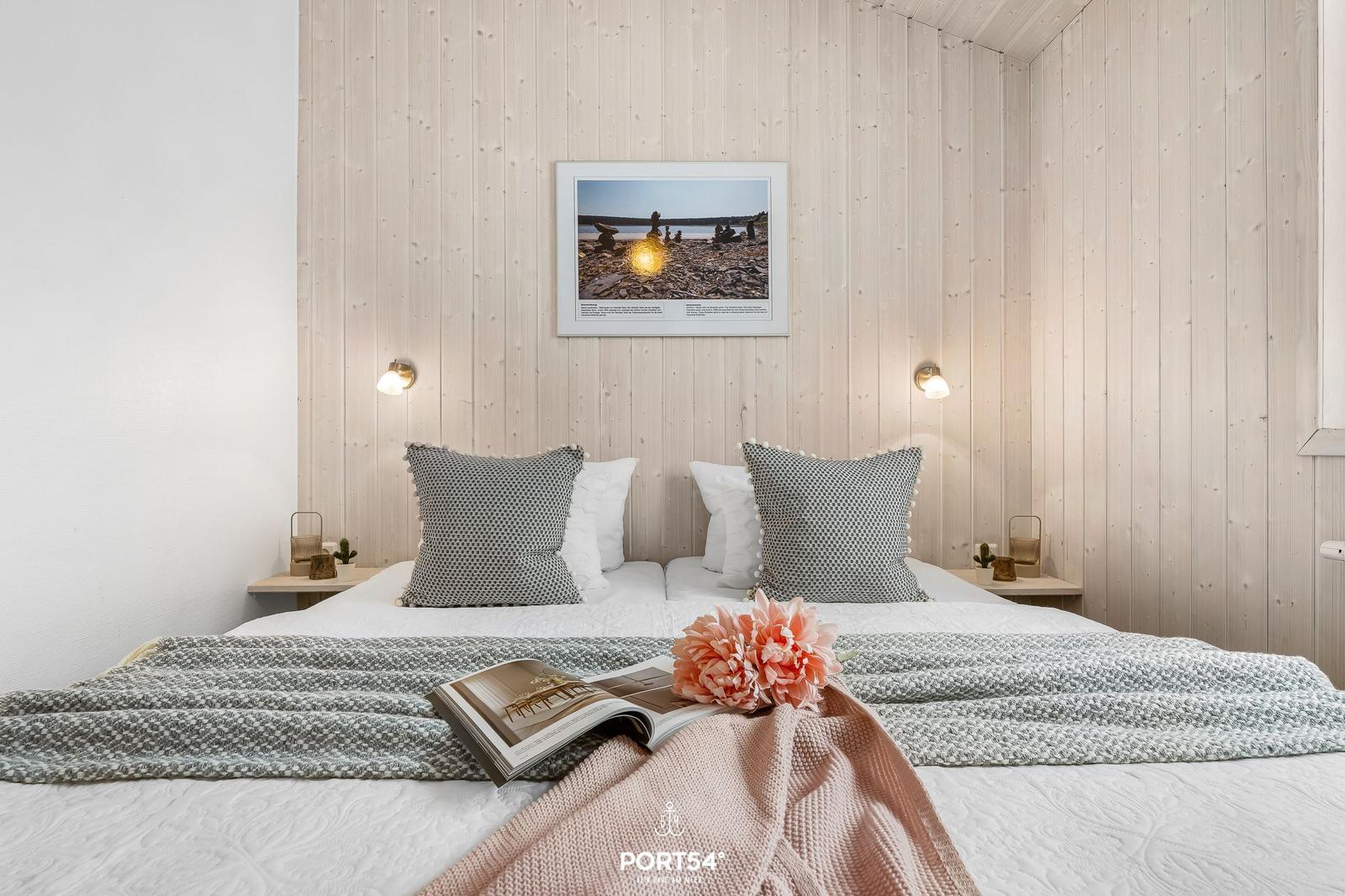 Schlafzimmer mit Holzwand, Bett, Kissen und Bild an der Wand.